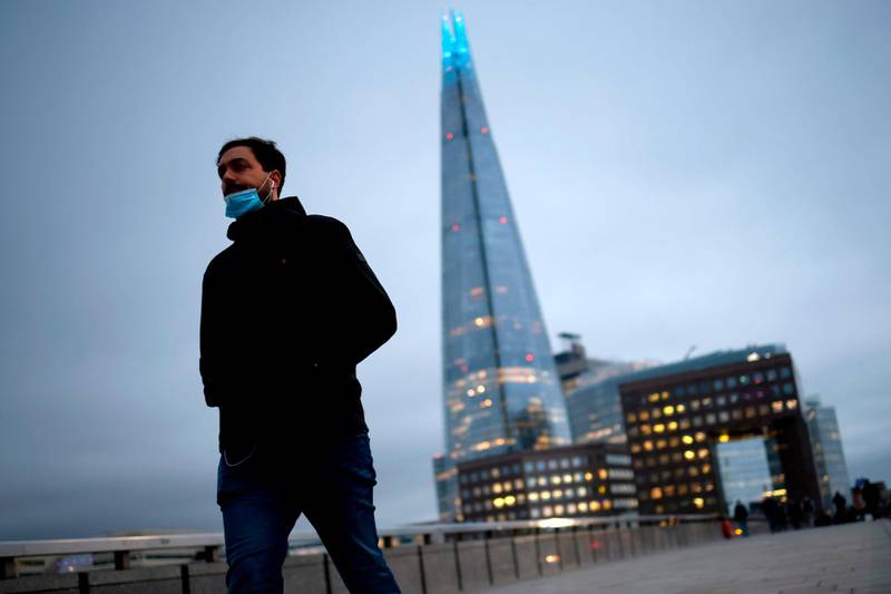 A pedestrian wearing a mask crosses London Bridge with the Shard tower in the background. AFP