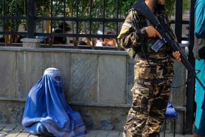 An Afghan woman begs as Taliban fighters stand guard in Kabul. Amnesty International says the Taliban have breached women's and girls' rights to education, work and free movement since they took control of the government. EPA
