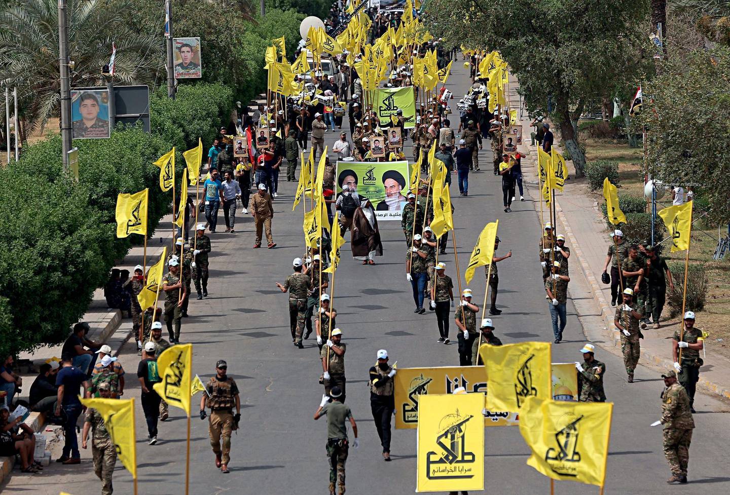 In this June 8, 2018 file photo, Iraqi Popular Mobilization Forces march as they hold their flag and posters of Iraqi and Iranian Shiites spiritual leaders during "al-Quds" or Jerusalem Day, in Baghdad, Iraq. The Trump administration will resume crushing oil sanctions on Iran in Nov. 2018, a step that aims to strain Tehranâ€™s funding of its regional allies. Iranian-backed militias in Iraq are buffered to an extent from any financial crunch because they also get funding from the Baghdad government, which is nominally a U.S. ally.  (AP Photo/Hadi Mizban, File)