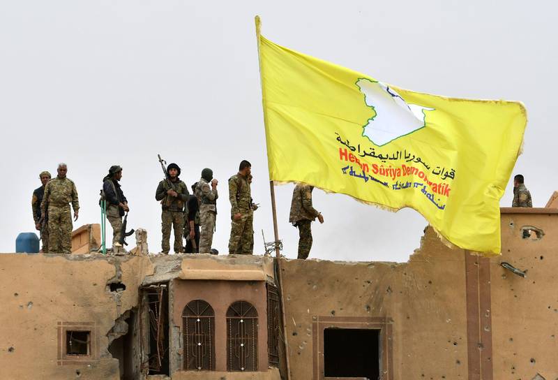 EDITORS NOTE: Graphic content / Fighters of the Syrian Democratic Forces (SDF) stand atop a roof next to their unfurled flag at a position in the village of Baghouz in Syria's eastern Deir Ezzor province near the Iraqi border on March 24, 2019, a day after the Islamic State (IS) group's "caliphate" was declared defeated by the US-backed Kurdish-led SDF. (Photo by GIUSEPPE CACACE / AFP)