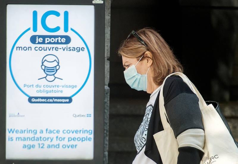 A woman wears a face mask as she walks by a sign advising of the mandatory wearing of masks and face coverings in Montreal, on 21 September. Graham Hughes/The Canadian Press via AP