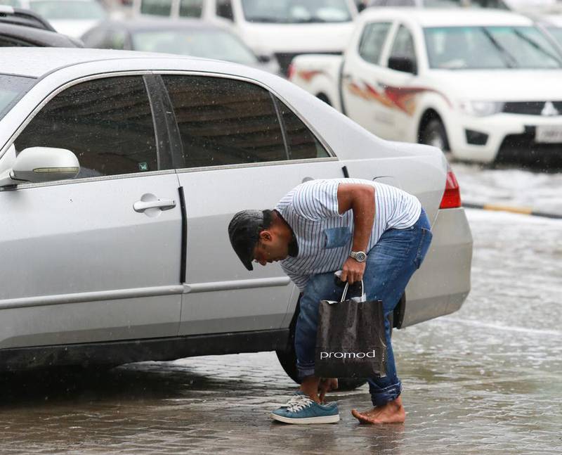 A pedestrian puts his shoes back on after crossing a flooded street in Sharjah. Victor Besa for The National