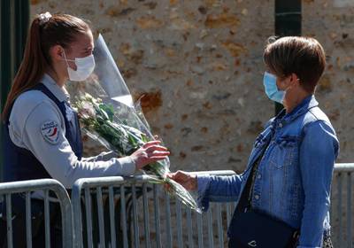 A woman hands flowers to a police officer to be taken down to the police station where a police official was stabbed to death Friday in Rambouillet, south west of Paris, Saturday, April 24, 2021. Anti-terrorism Investigators were questioning three people Saturday detained after the deadly knife attack a day earlier on a police official at the entry to her station in the quiet town of Rambouillet, seeking a motive, purported ties to a terrorist group and whether the attacker, killed by police, acted alone. (AP Photo/Michel Euler)