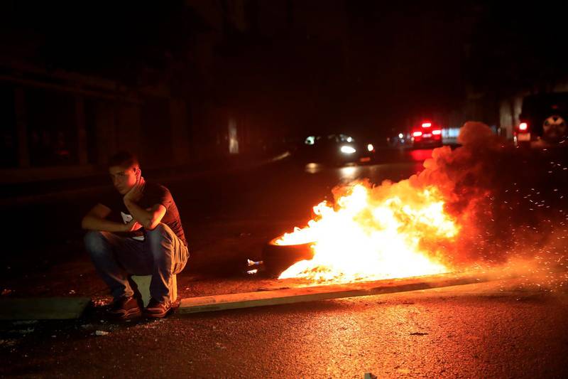 A protester in Beirut sits next to burning tires, as he blocks a main street by burning tires, after a top court suspended a Central Bank decree that allowed the Lebanese to withdraw from dollar deposits at a rate two and a half times better than the fixed exchange rate. AP Photo