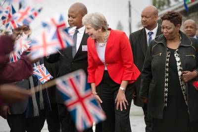 TOPSHOT - Britain's Prime Minister Theresa May (C) is greeted by schoolchildren waving British and South African flags, during a visit to the ID Mkhize Secondary School in Gugulethu township, about 15 km from the centre of Cape Town, on August 28, 2018, as part of a three-nation visit to Africa in Cape Town where she is expected to discuss post-Brexit trade ties with the continent's most developed economy. (Photo by Rodger BOSCH / POOL / AFP)