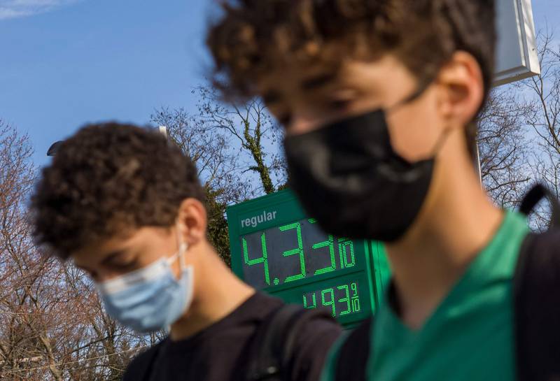 Two people wearing masks walk in front of a sign showing the price of petrol outside of a station as prices reach record highs in Washington. AFP