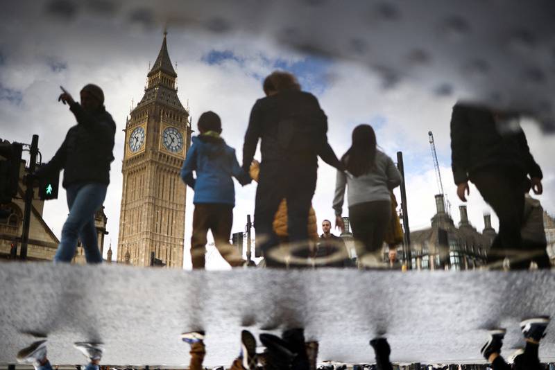 Big Ben is  reflected in a puddle as pedestrians pass the Houses of Parliament in London.  Reuters