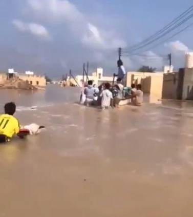 Residents wade through flood waters in in the coastal town of Ras Al Hadd, about 100km south of Muscat, on Tuesday morning
