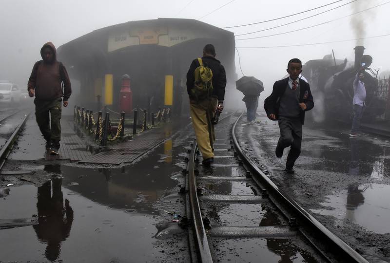 People cross the narrow-gauge tracks as a Darjeeling Himalayan Railway train prepares to depart from a station in Ghum.