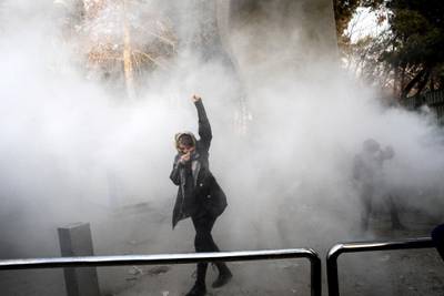 In this photo, a university student attends a protest inside University of Tehran while a smoke grenade is thrown by anti-riot police on December 30. AP