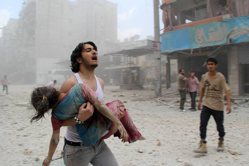 EDITORS NOTE: Graphic content / (FILES) In this file photo taken on June 3, 2014, a man carries a young girl who was injured in a reported barrel-bomb attack by government forces, in Kallaseh district in the northern city of Aleppo. As it enters its tenth year, the war in Syria is anything but abating as foreign powers scrap over a ravaged country where human suffering keeps reaching new levels. / AFP / BARAA AL-HALABI
