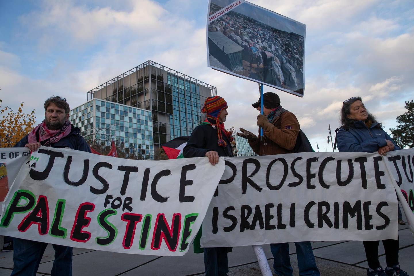 Demonstrators carry banners outside the International Criminal Court, ICC, rear, urging the court to prosecute Israel's army for war crimes in The Hague, Netherlands, Friday, Nov. 29, 2019. The ICC prosecutor was directed to reconsider her decision to not pursue charges in the Gaza Freedom Flotilla case. (AP Photo/Peter Dejong)