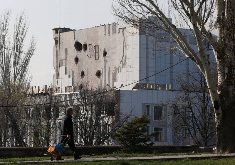 A local resident of Mariupol walks past the Palace of Culture, which was damaged during the conflict. Reuters