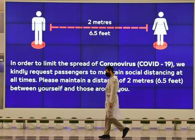 An Employee at Dubai International Airport, walk past a poster reminding passengers to keep a safe distance from each other, after the resumption of scheduled operations by the Emirati carrier, amid the ongoing novel coronavirus pandemic crisis, on May 22, 2020.




  / AFP / Karim SAHIB
