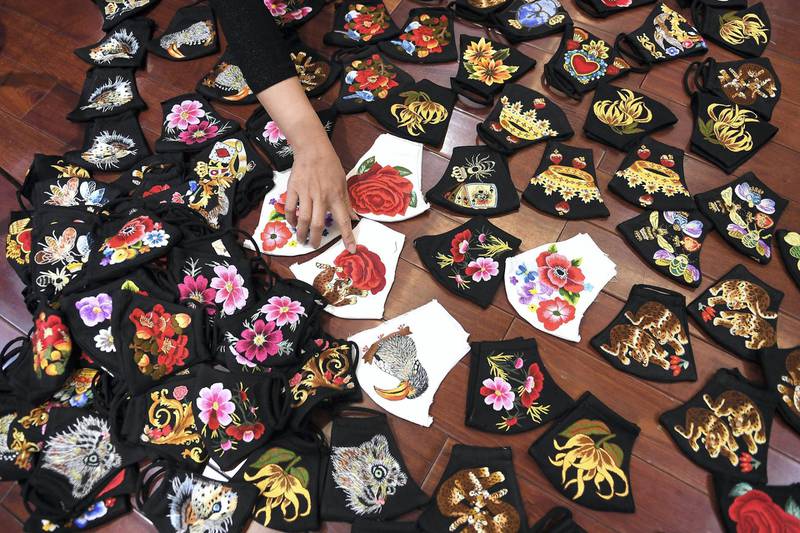 A worker points at colourful hand-embroidered face masks, used as a preventive measure against the spread of the COVID-19 novel coronavirus, at designer Do Quyen Hoa's workshop in Hanoi on April 13, 2020. (Photo by Nhac NGUYEN / AFP)