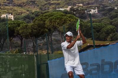 Coach Marco Villiegas plays tennis at the Overhead Tennis Academy against a charred backdrop.