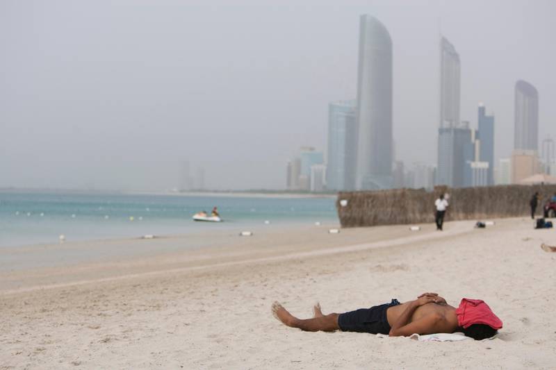 A man covers his face to protect against the sun, and sand swirling in the air at the Public Beach in Abu Dhabi, United Arab Emirates on Saturday April, 6, 2013.  RJ Mickelson / The National