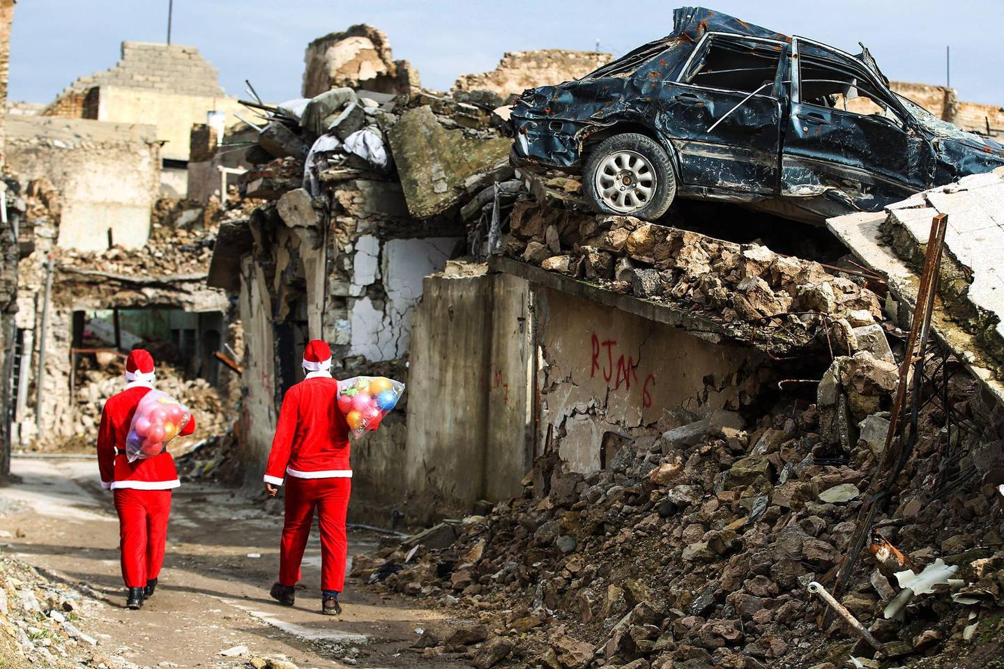 TOPSHOT - Iraqi youths dressed in Father Christmas suits walk through the streets of the old city of Mosul as they distribute gifts, on December 26, 2018. Iraq on December 10 marked the first anniversary since declaring victory in its three-year war against the Islamic State (IS) group, which had left the country's former second city and the jihadists' capital in ruin. / AFP / AHMAD AL-RUBAYE
