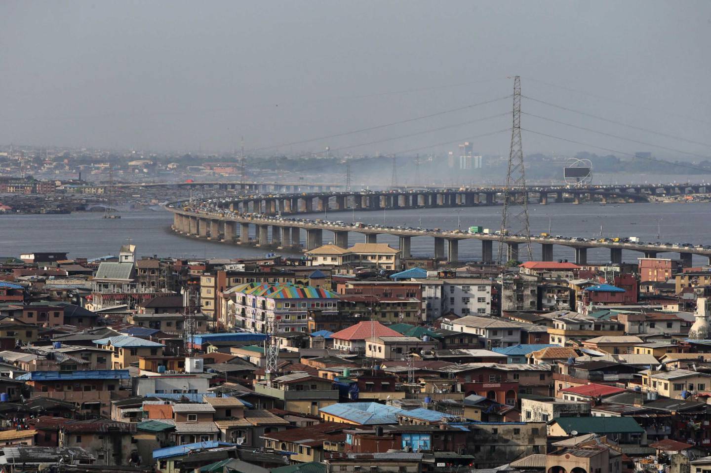 An electricity pylons carries power cables above residential property as traffic passes across a bridge from Isale Eko on Lagos Island towards the mainland in Lagos, Nigeria, on Monday, Oct. 26, 2015. Nigeria plans to create a $25 billion fund with public and private financing to modernize infrastructure and avoid a recession, Vice President Yemi Osinbajo said. Photographer: George Osodi/Bloomberg