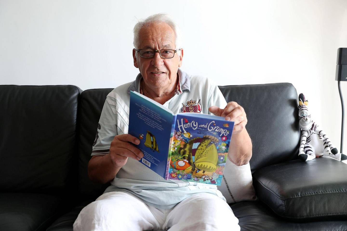 DUBAI , UNITED ARAB EMIRATES , December 11  – 2018 :- John Felton, a retired lawyer who is now a children’s author with one of his book at his apartment at the Cayan Tower  in Dubai Marina in Dubai. ( Pawan Singh / The National ) For Business. Story by David