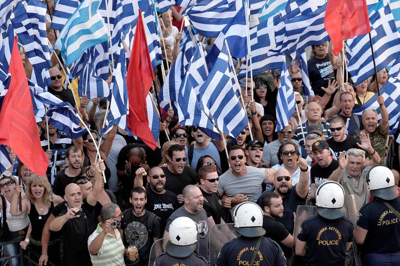 Supporters of the far right Golden Dawn party wave flags and shout slogans outside the Athens Appeals Court as a police van brings their jailed leader Nikos Michaloliakos, his second-in-command Christos Pappas and another MP, Yiannis Lagos, on July 4, 2014 in Athens to defend themselves before the magistrates leading a probe into the neofascist party on additional charges .  AFP PHOTO / LOUISA GOULIAMAKI (Photo by LOUISA GOULIAMAKI / AFP)