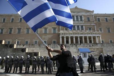 A farmer waves a Greek flag in front of riot police standing guard in front of the parliament on November 18, 2015, during an anti-government protest at central Syntagma square in Athens. Greek farmers protesting over planned tax and pension reforms demanded by the country’s bailout creditors have clashed outside parliament with police, who used tear gas to disperse them. Yorgos Karahalis / Associated Press