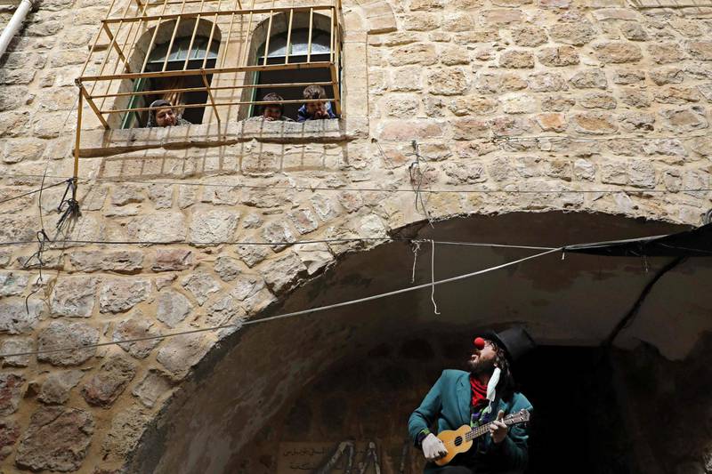 Palestinian artist Ameer Abu Ghalioon plays music dressed as a clown under the windows of Palestinian families keeping the confinement in the divided West bank town of Hebron.  AFP