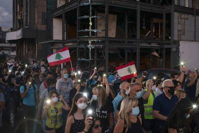 Demonstrators march past a damaged building holding candles and flashlights honouring the victims. AP