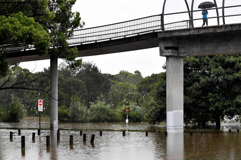 A resident uses a pedestrian bridge as floodwaters inundate residential areas in south-west Sydney. AFP