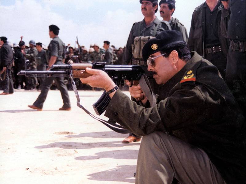 Saddam Hussein points a Kalashnikov at an unspecified location in Iraq, 1987. AFP