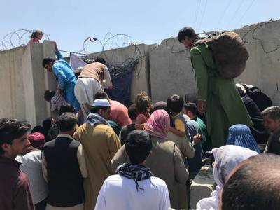 People climb a wall at Hamid Karzai International Airport in desperation after rumours that foreign countries were flying Afghans out after the Taliban overran Kabul on Monday. Getty