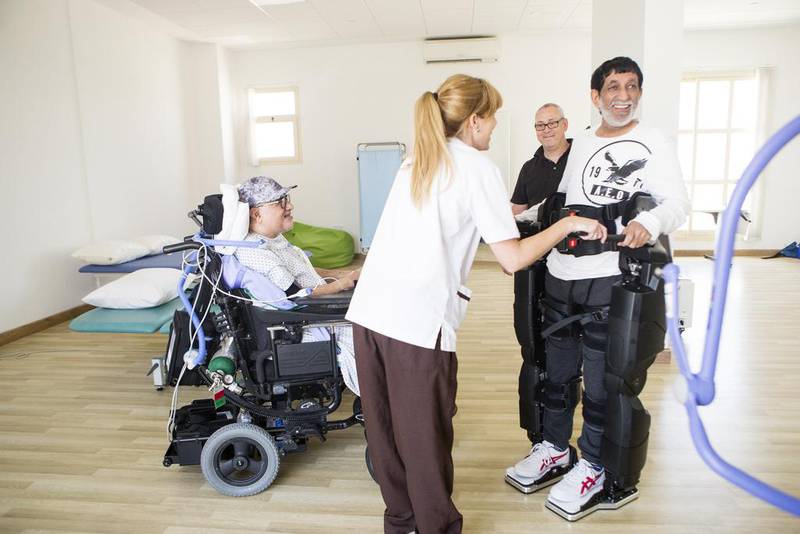 Physiotherapist Sarah McGloughlin works with stroke sufferer Abdulrahman Al Yousef, 53, using the Rex Bionics robotic exoskeleton. Also pictured is Ali Ahmed Saleh Al Mehrezi, who uses the unit for rehab after suffering a spinal injury. Christopher Pike / The National