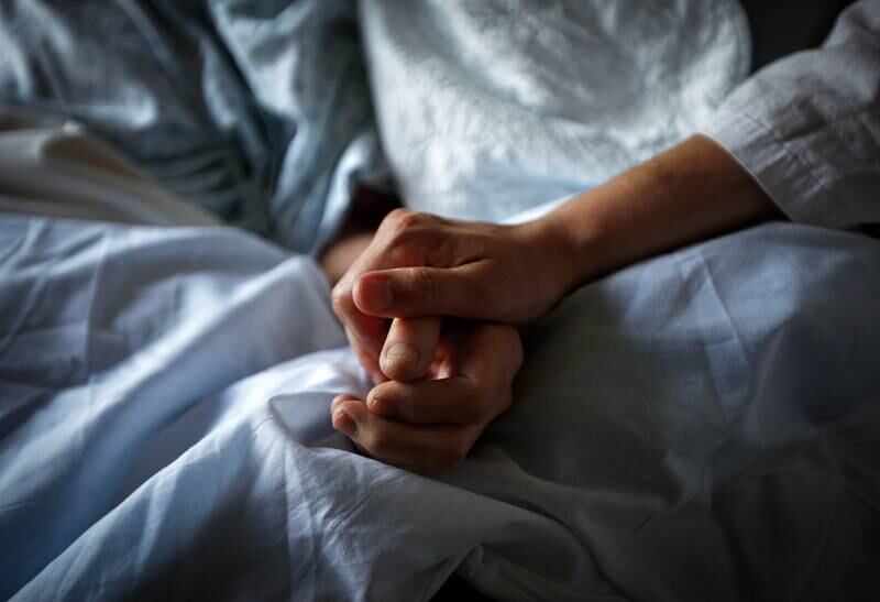 A woman holds the hand of her mother who is dying from cancer. Reuters