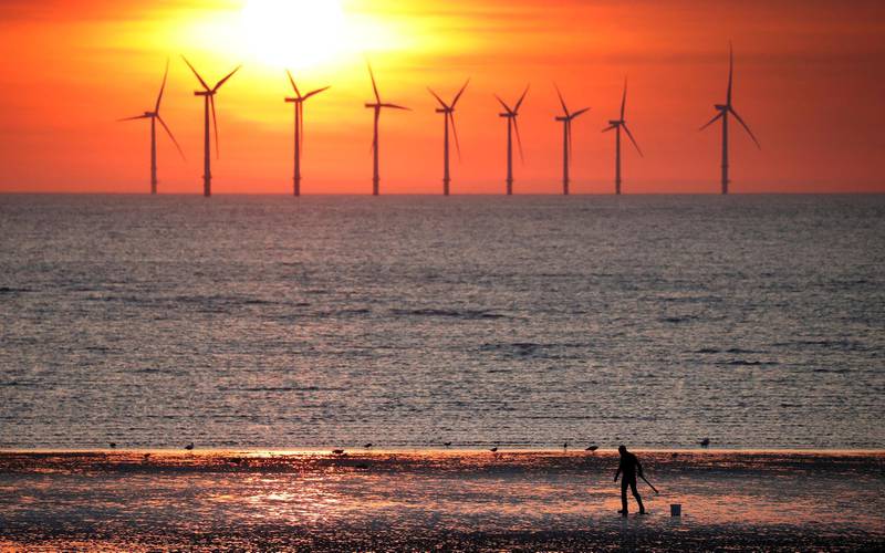 FILE PHOTO: A man stands on the beach as the sun sets behind the Burbo Bank wind farm near New Brighton, Britain, May 22, 2018. REUTERS/Phil Noble/File Photo