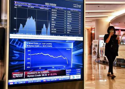 A woman wearing a face mask walks past an electronic board showing Asian stock indexes at a shopping mall in Bangkok.  AFP