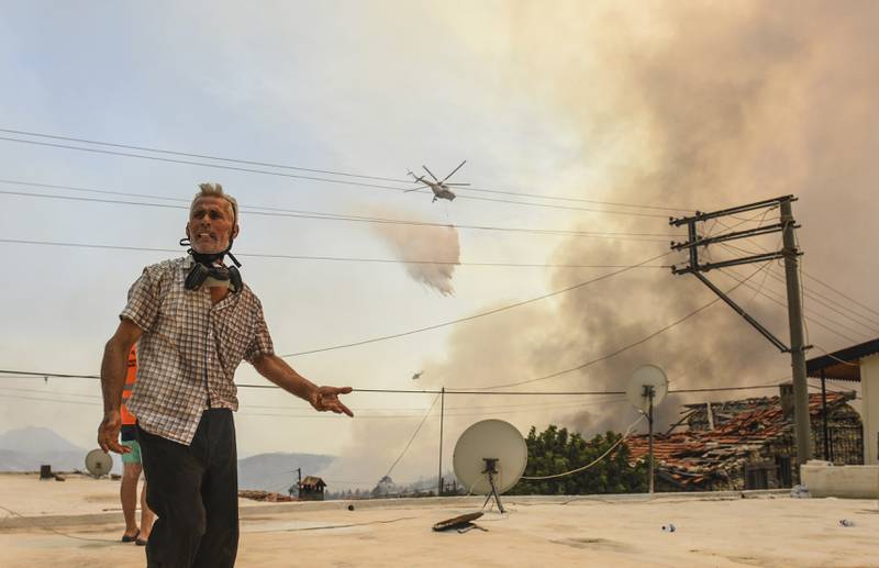 A man reacts as a helicopter pours water over Sirtkoy, a village near Manavgat.