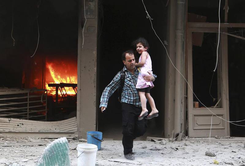 A man carrying a child runs out of a burning building at a site hit by what activists said were barrel bombs dropped by forces of Syria’s President Bashar al-Assad in Aleppo’s al-Shaar district. Hamid Khatib / Reuters