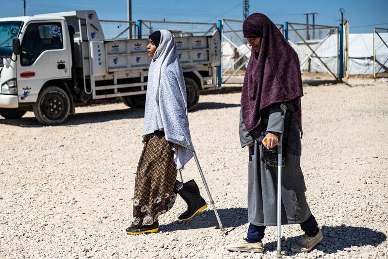 Two women walk with the aid of crutches through the camp. AFP