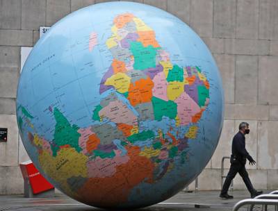 A man wearing a face mask walks past a globe in front of the London School of Economics in London. AP Photo