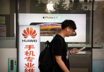 A man looks at his smartphone as he walks past an electronics shop advertising phones from Huawei and Apple in Beijing, Friday, May 24, 2019. Stepping up a propaganda offensive against Washington, China's state media on Friday accused the U.S. of seeking to "colonize global business" by targeting telecom equipment giant Huawei and other Chinese companies. (AP Photo/Mark Schiefelbein)