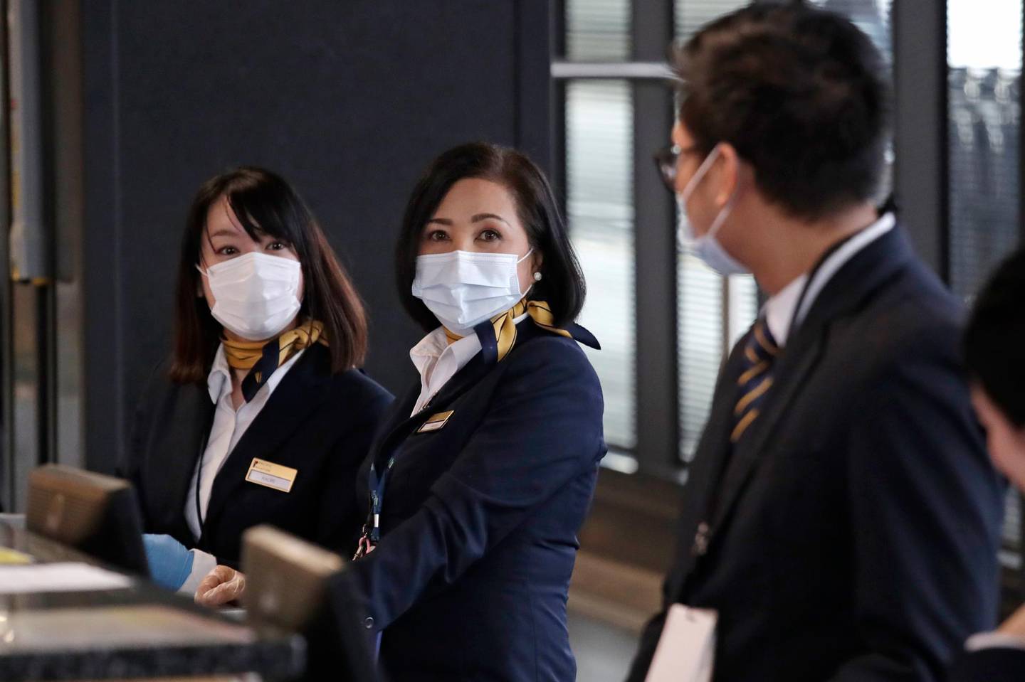 Japan Airlines ticket agents wear masks as they wait for the few passengers flying with them at Seattle-Tacoma International Airport Wednesday, April 15, 2020, in SeaTac, Wash. Flights at the usually busy airport have dropped from up to 1,300 a day to about 400 each day. (AP Photo/Elaine Thompson)