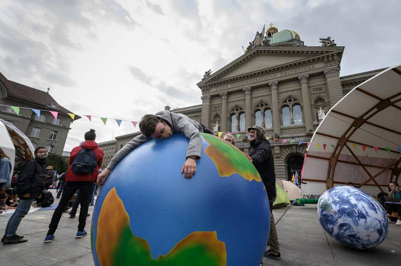 A climate activist lays on an inflatable world globe in front of the Swiss House of Parliament at the start of a week of demonstrations called "Rise up for change" on September 21, 2020 in Bern.   / AFP / Fabrice COFFRINI
