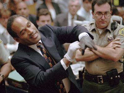 FILE - In this June 15, 1995 file photo, O.J. Simpson, left, grimaces as he tries on one of the leather gloves prosecutors say he wore the night his ex-wife Nicole Brown Simpson and Ron Goldman were murdered in a Los Angeles courtroom. Simpson, the former football star, TV pitchman and now Nevada prison inmate, will have a lot going for him when he appears before state parole board members Thursday, July 20, 2017, seeking his release after more than eight years for an ill-fated bid to retrieve sports memorabilia. (AP Photo/Sam Mircovich, Pool, file)