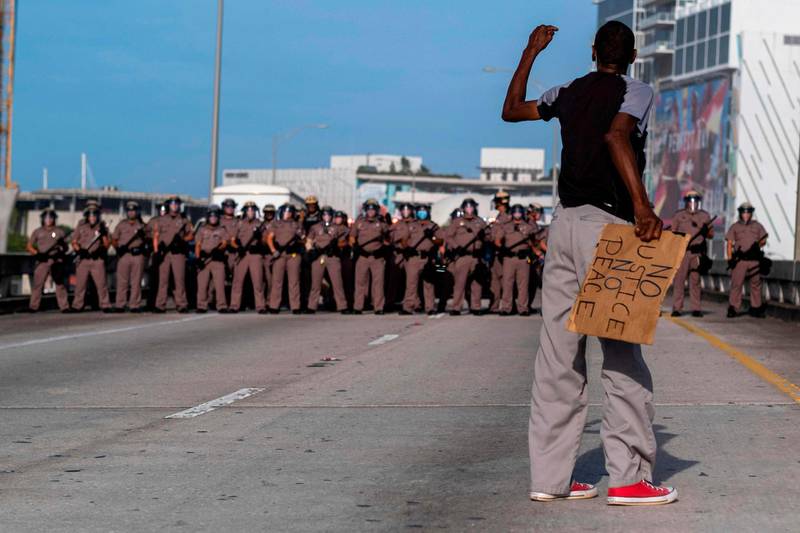 A protestr holding a "No Justice No Peace" sign shouts at Florida State Troopers. AFP