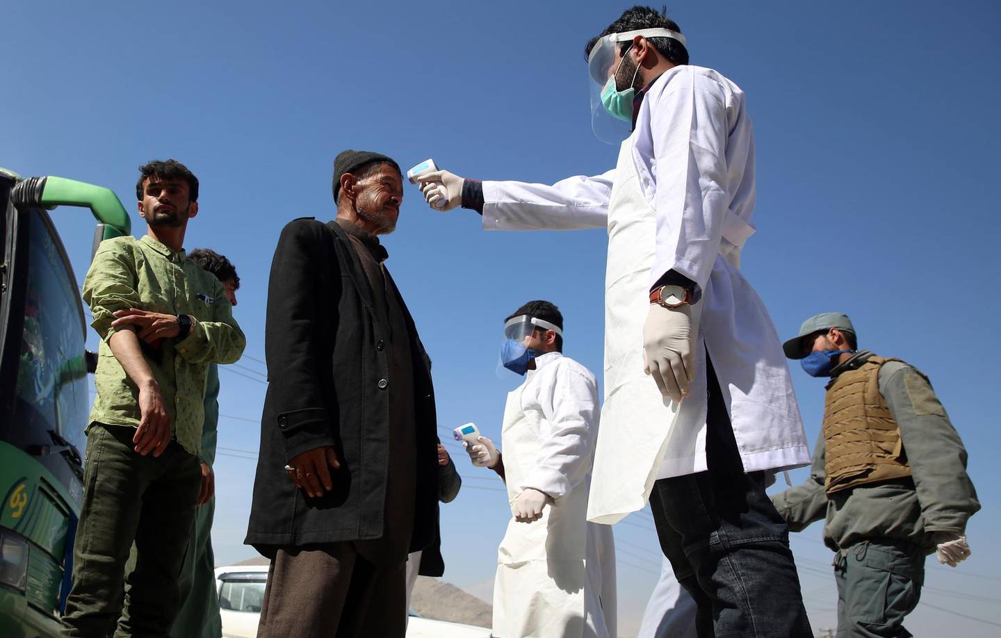 FILE - In this Sunday, March 22, 2020 file photo, health workers measure the temperature of Afghan passengers in an effort to prevent the spread of the coronavirus, as they enter Kabul trough Kabul's western entrance gate, in the Paghman district of Kabul, Afghanistan. Some 200,000 Afghans and counting have returned from Iran to their home country after losing their jobs in the coronavirus pandemic or out of fear of getting infected. They are flowing across the border from a country that has one of the world's worst outbreak to an impoverished nation that is woefully unprepared to deal with the virus. (AP Photo/Rahmat Gul, File)
