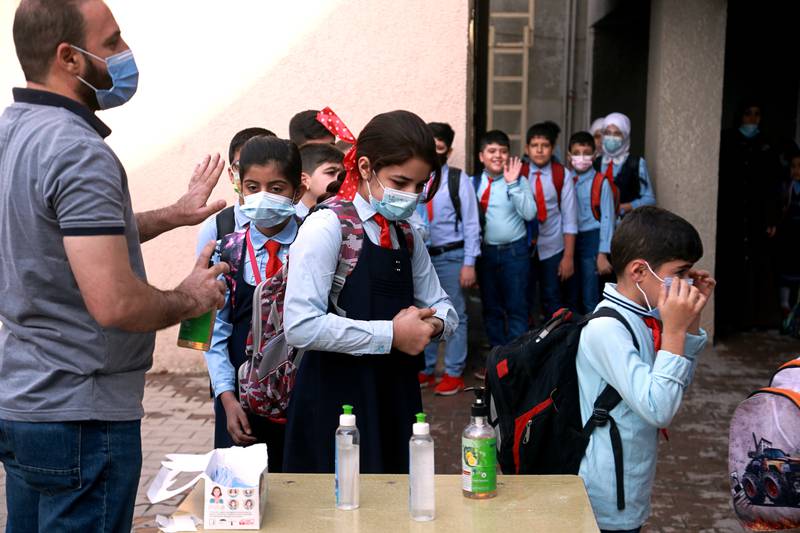 A teacher sanitises pupils' hands in the playground at a school in Baghdad, one of the many anti-coronavirus measures. AP