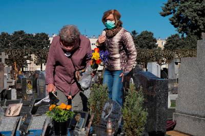 Two women wearing face masks lay flowers on a grave in Tours Saint-Symphorien cemetery, exceptionally open for Palm Sunday (Dimanche des Rameaux) on April 5, 2020, on the twentieth day of a lockdown in France aimed at curbing the spread of the COVID-19 infection caused by the novel coronavirus. / AFP / GUILLAUME SOUVANT
