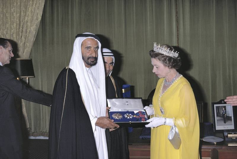 Queen Elizabeth ll appoints Sheikh Rashid bin Saeed Al Maktoum (1912-1990), the ruler of Dubai, a Knight Grand Cross of the Order of Saint Michael and Saint George, as part of her tour of the Gulf States, in Abu Dhabi, United Arab Emirates, on 25 February 1979. Prince Philip stands to the back left of the image. (Photo by Tim Graham/Getty Images)