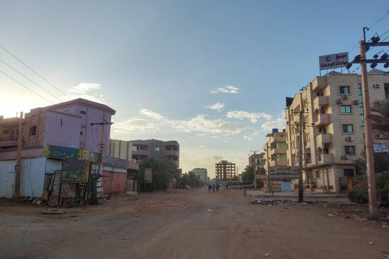 People walk along a mostly deserted street in southern Khartoum, as smoke from fighting rises in the distance. AFP