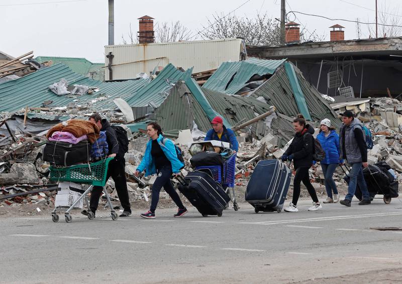Residents carry belongings past a destroyed building in Mariupol. Reuters